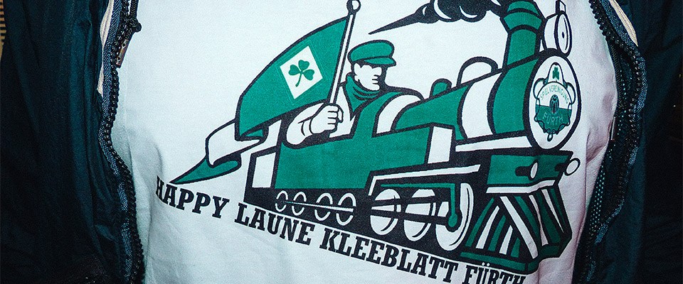 T-Shirt mit dem Aufdruck "Happy Laune Kleeblatt Fürth" unter dem Bild einer weiß-grünen Dampflokomotive.